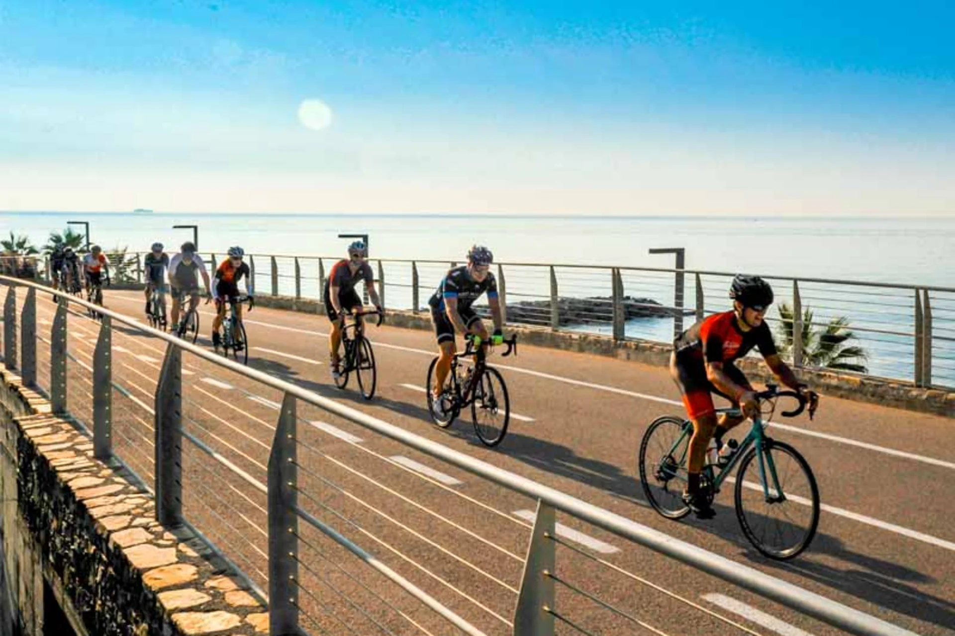 Roadbike Holidays © Villa Giada spEace & Bike Resort Gruppe von Radfahrern fährt an der Meerespromenade bei sonnigem Wetter