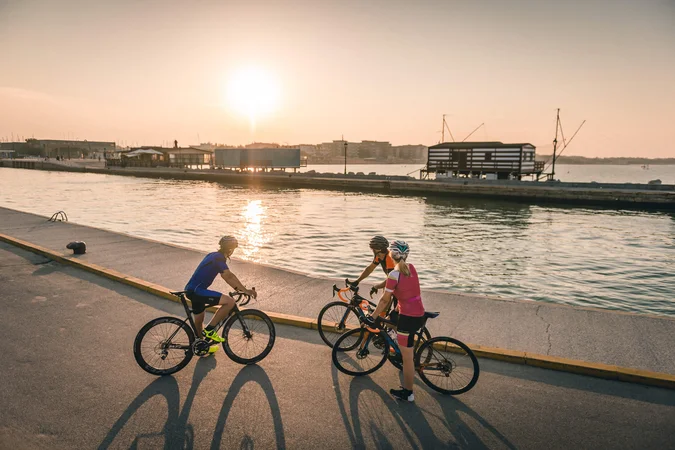 Roadbike Holidays © Alex Moling Drei Radfahrer stehen bei Sonnenuntergang an einem Wasserweg