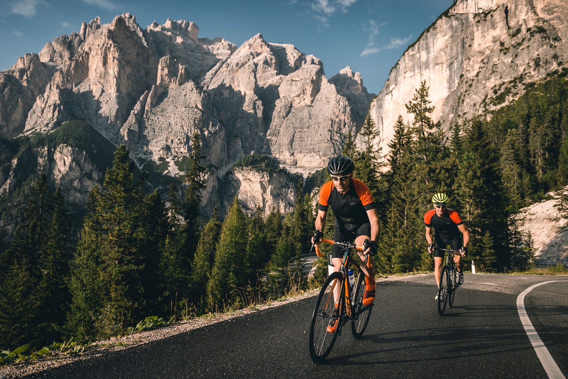 Roadbike Holidays © Molography Zwei Radfahrer fahren auf Bergstraße mit Felsen und Nadelbäumen im Hintergrund