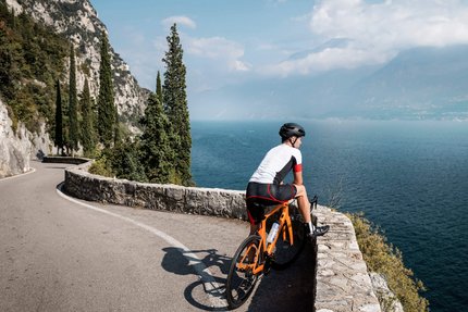 Tour del Lago di Garda © Alex Moling Radfahrer auf kurviger Straße mit Blick auf See und Berge