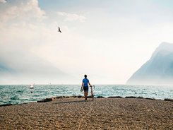 Nördlicher Gardasee © Alex Moling Fahrradfahrer am Seeufer mit Bergen und Segelbooten im Hintergrund