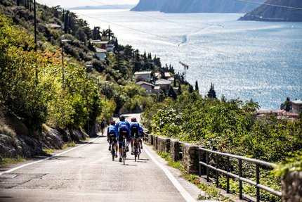Monte Baldo © Castelli Drei Radfahrer fahren auf einer Straße entlang eines Sees mit Bergen im Hintergrund