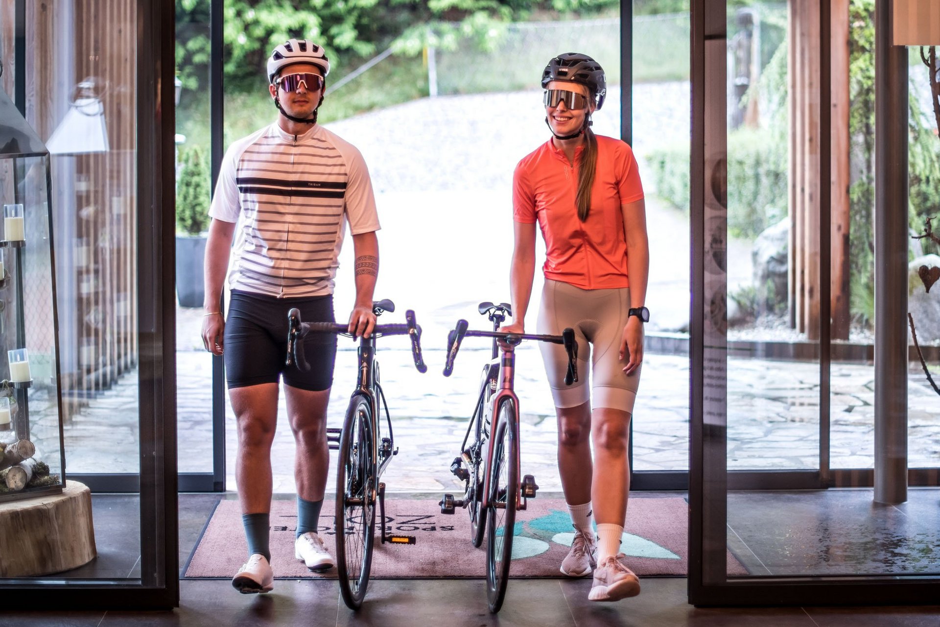 Roadbike Holidays © Fabian Schaiter Zwei Radfahrer mit Helmen und Fahrrädern in einem modernen Gebäude