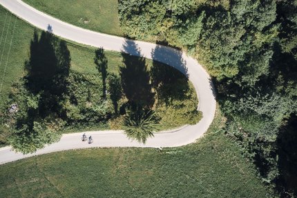 Baden-Württemberg © Tobias Köhler Luftaufnahme von zwei Radfahrern auf geschwungener Straße durch grüne Landschaft