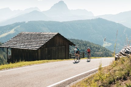 Brixen & Würzjoch © Alex Moling Two cyclists riding on mountain road next to wooden hut in the Alps