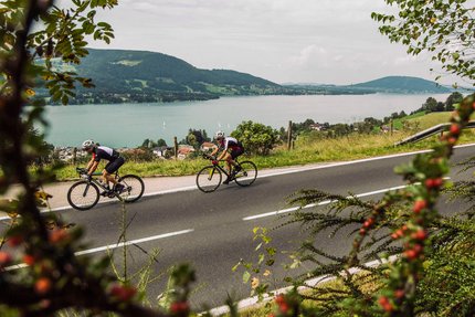 Attersee - Rundweg über Mondsee © SalzburgerLand - Stefan Schopf for WOM Medien Zwei Radfahrer auf Landstraße mit Berg- und Seeblick