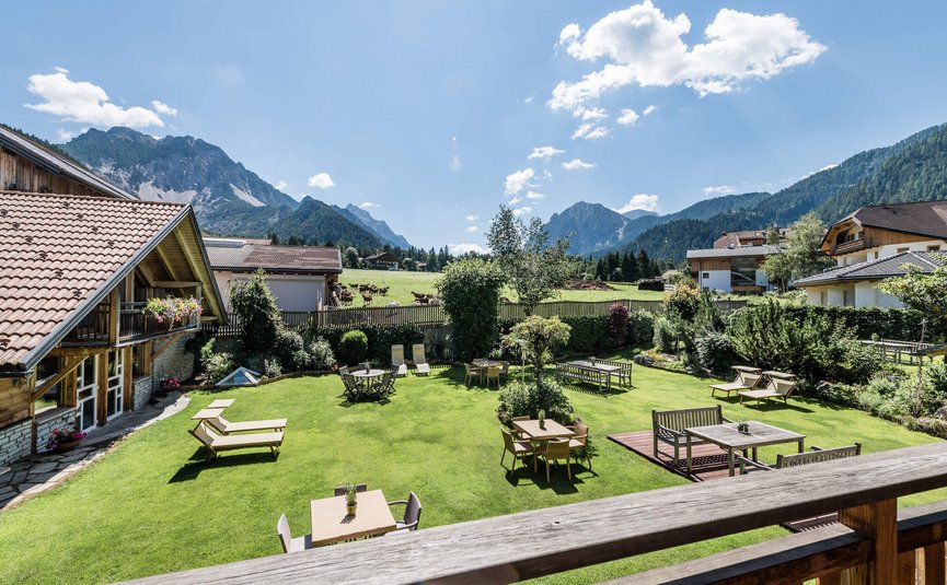 Sporthotel Exclusive **** © Sporthotel Exclusive SAS Garden with tables and lounge chairs in front of mountains under clear sky