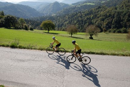 Seebergsattel © Kaja Ribezl Zwei Radfahrer fahren auf Landstraße vor grünen Hügeln und Bergen