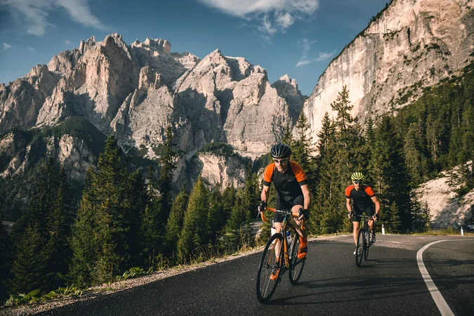 Roadbike Holidays © Molography Zwei Radfahrer fahren auf Bergstraße mit Felsen und Nadelbäumen im Hintergrund