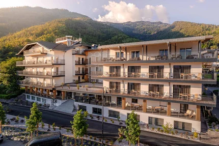 Cristallo Sport & Wellness Hotel © Andrea Acler Modernes Hotelgebäude mit Balkonen vor bewaldeten Bergen bei Sonnenlicht