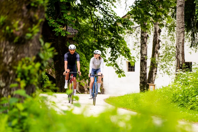 Roadbike Holidays © Michael Stabentheiner Zwei Fahrradfahrer auf einem Waldweg neben Bäumen und einer weißen Wand