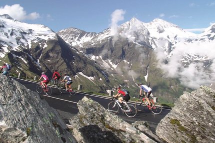 Grossglockner Hochalpenstrasse mit Abstecher nach Döllach © Sportcamp Woferlgut Bruck Radfahrer fahren auf Bergstraße mit schneebedeckten Alpen im Hintergrund