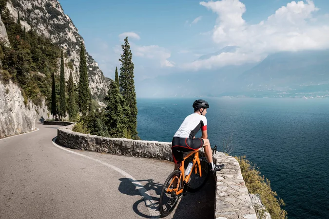 Roadbike Holidays © Alex Moling Radfahrer auf kurviger Straße mit Blick auf See und Berge