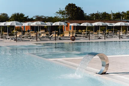 Natural Village Resort © Luigi Ventimiglia Leerer Pool mit Wasserfontäne und Sonnenschirmen am Nachmittag