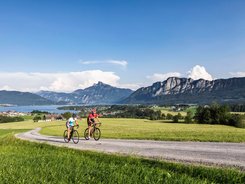 Rennradregion SalzburgerLand - Salzkammergut © TVB Mondsee Irrsee - Valentin Weinhaeupl Zwei Radfahrer fahren auf Landstraße mit Bergen und See im Hintergrund