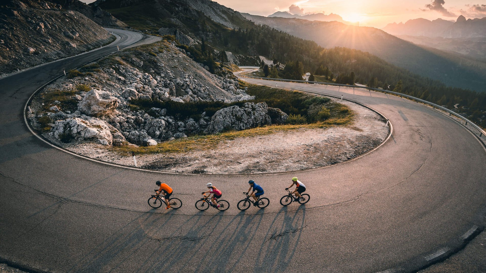 Roadbike Holidays © Molography Vier Radfahrer fahren auf gebirgiger Straße bei Sonnenuntergang