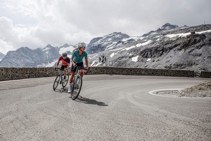 Grenzenlose Abenteuer in der Region Nauders - Reschensee © Felix Saller Zwei Radfahrer fahren eine Bergstraße mit schneebedeckten Gipfeln im Hintergrund