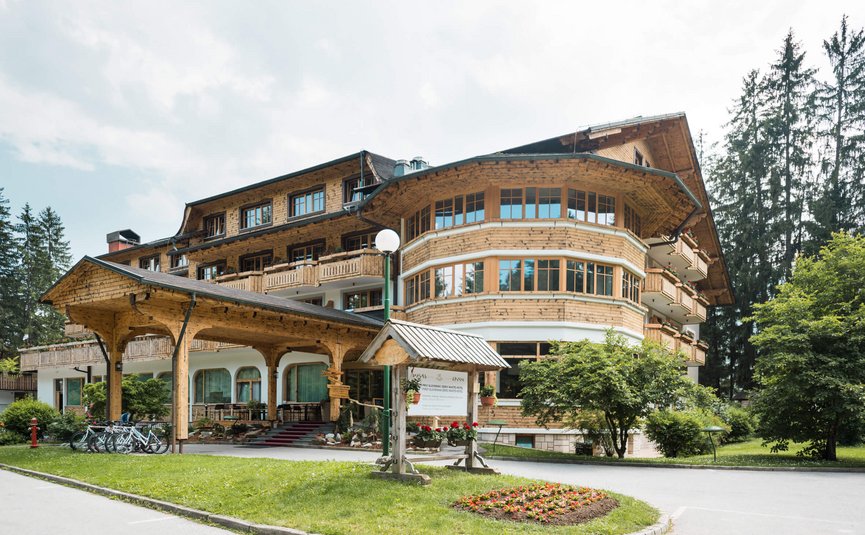 Hotel & Glamping Ribno Alpine Resort **** © Epidos doo Großes Holz-Hotelgebäude mit Vorbau und Fahrradständer in einem grünen Umfeld