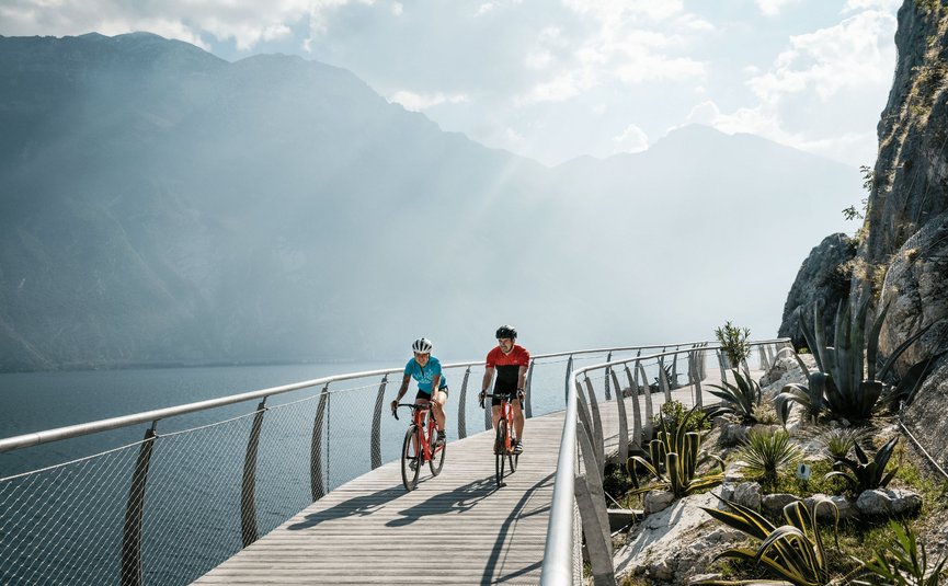 Racefietsvakantie aan het noordelijke Gardameer © Alex Moling Twee fietsers op een steiger bij het meer met bergen op de achtergrond