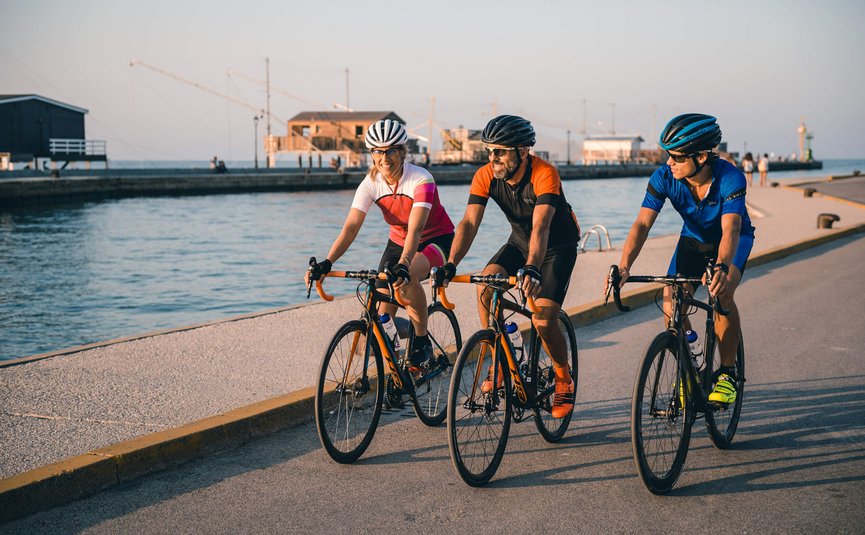 Road bike holidays on the Adriatic coast © Alex Moling Three cyclists in colorful outfits riding bikes along waterfront on clear day