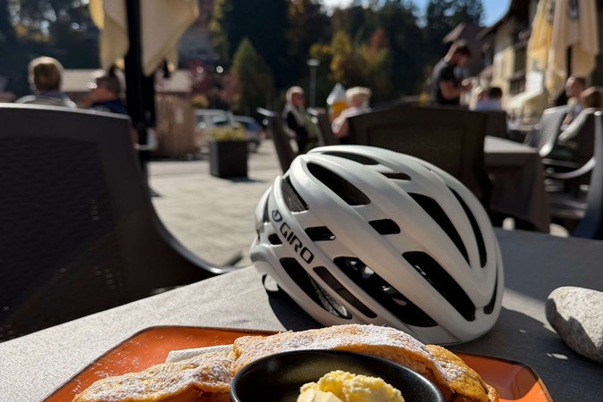 Roadbike Holidays Apfelstrudel mit Vanilleeis auf orangefarbenem Teller neben Fahrradhelm im Außenbereich