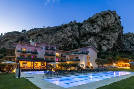 Triathlon & Rennrad Aktivhotel SantaLucia © Fabio Staropoli Hotel mit beleuchtetem Pool vor einem großen Felsen bei Abenddämmerung