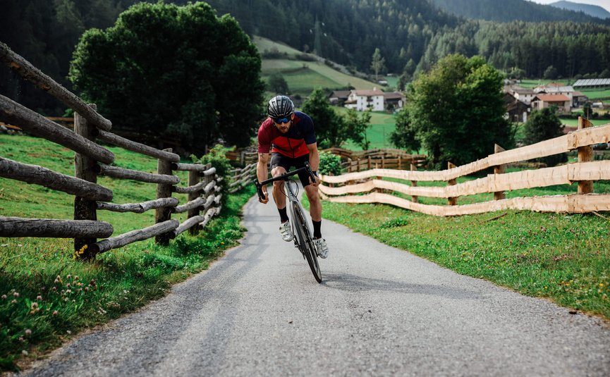 Vacanze in bici da corsa nella regione di Nauders – Lago di Resia © Felix Saller Uomo in bici da corsa su strada di campagna con recinzioni in legno e montagne