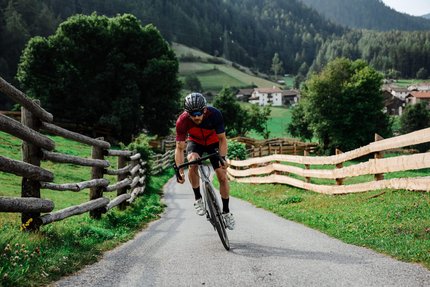 Passo Flüela © Felix Saller Uomo in bici da corsa su strada di campagna con recinzioni in legno e montagne