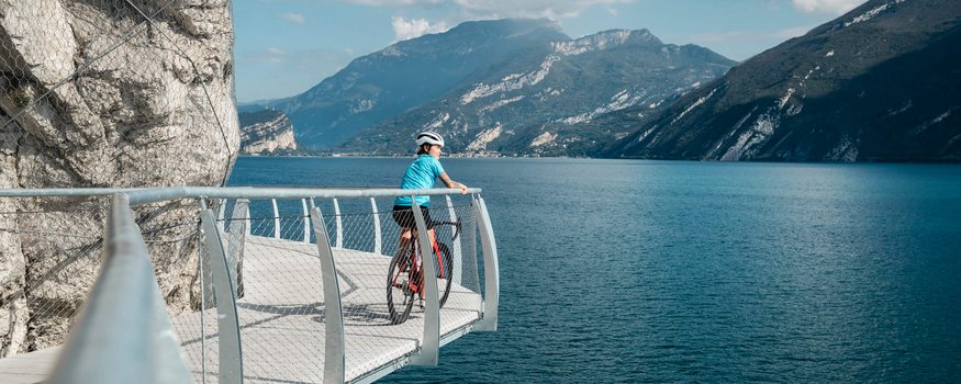 Noordelijke Gardameer © Alex Moling Fietser op wandelpad met uitzicht op meer en bergen bij zonnig weer