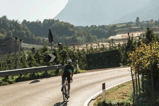 Roadbike Holidays © marc.moves x velysiped Radfahrer auf einer kurvigen Landstraße mit Bergen im Hintergrund