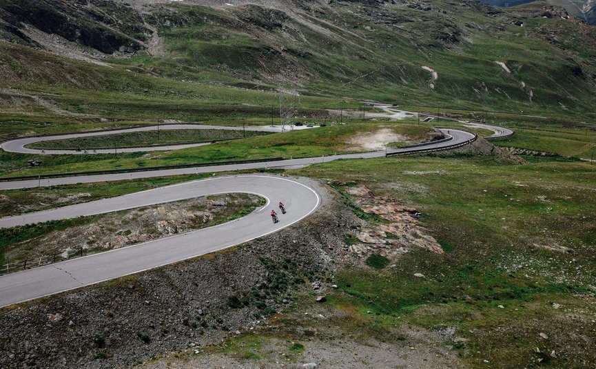 Vacanze in bici da corsa nella regione di Nauders – Lago di Resia © Felix Saller Due ciclisti su strada tortuosa in montagna con paesaggio verde