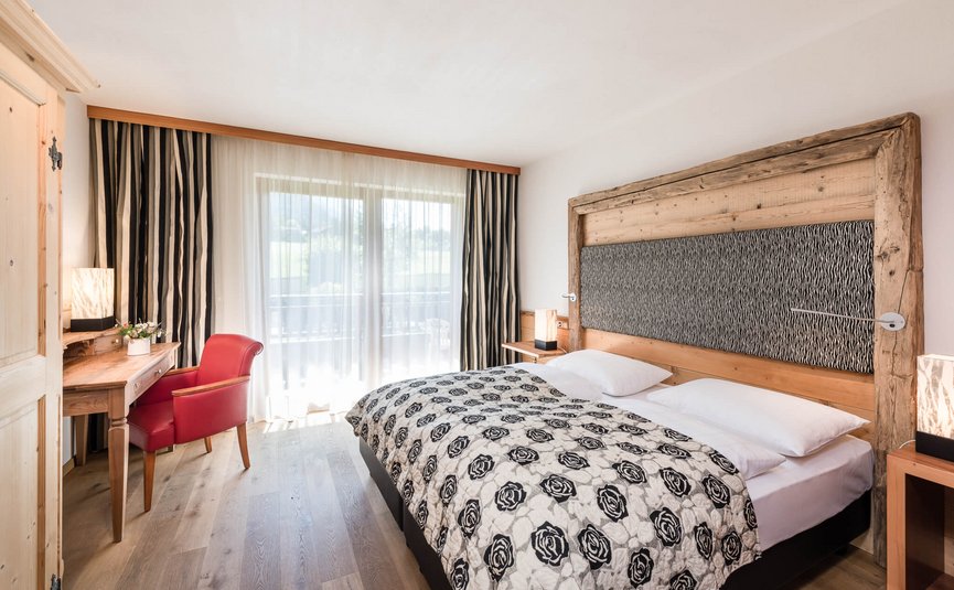 Sporthotel Exclusive **** © Sporthotel Exclusive SAS Bright bedroom with large bed, wooden decor and red chair