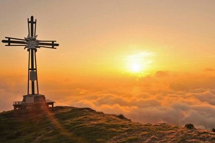 Kleine Kitzbühel Runde © Sportcamp Woferlgut Bruck Holzkreuz auf Berggipfel bei Sonnenaufgang über Wolken