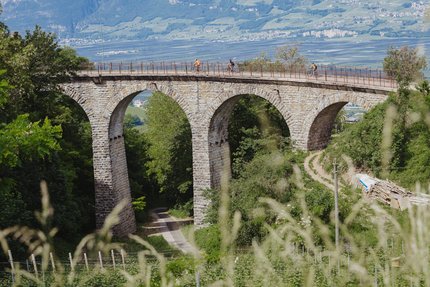 Kurven, Kultur & Kontraste in Südtirols Süden © Thomas Monsorno - TV Castelfeder Fahrradfahrer auf einer Steinbrücke mit Bögen in einer grünen Landschaft