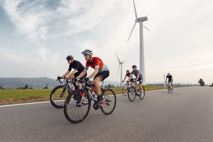 Sachsen © Felix Meyer Fünf Radfahrer fahren auf einer Straße mit Windkraftanlagen im Hintergrund