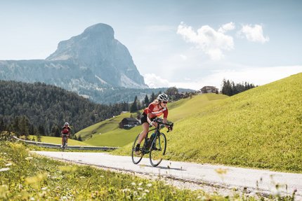 Zwischen Pass & Pasta in San Vigilio © Alex Moling Zwei Radfahrer fahren auf Bergstraße mit Gipfel in der Sonne