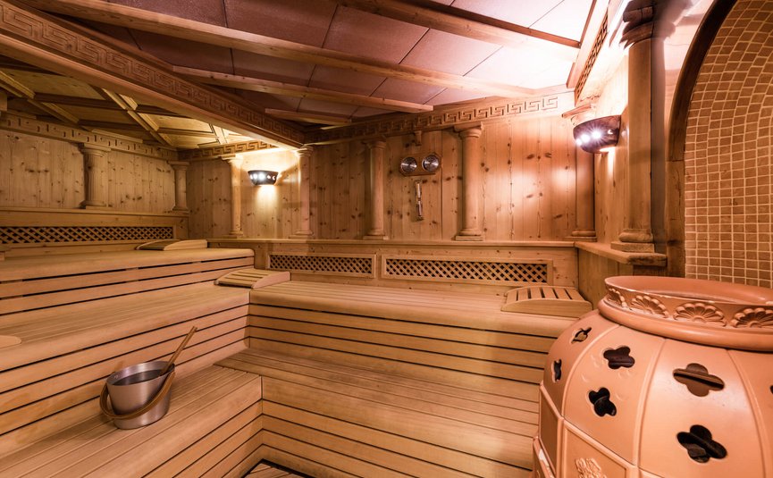 Sporthotel Exclusive **** © Sporthotel Exclusive SAS Sauna room with wooden benches and stove in warm lighting