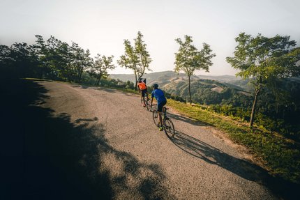 Bertinoro © Alex Moling Two cyclists riding on a winding road with trees and hills in the background