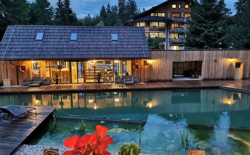 Hotel & Glamping Ribno Alpine Resort **** © Katarina Strgar Beleuchteter Holzpoolbereich mit Sitzgelegenheiten und Gebäude im Wald am Abend