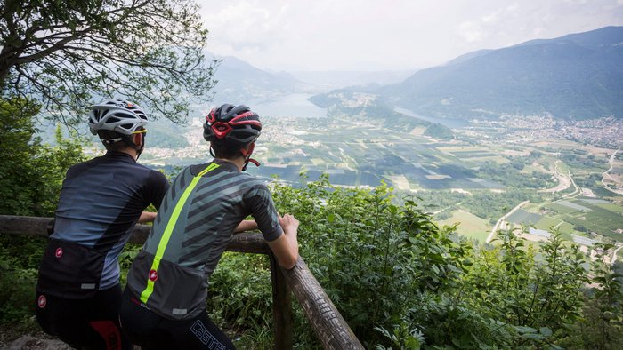 Tours & Travels © Heiko Mandl Two cyclists looking over a valley and mountains from a green viewpoint.