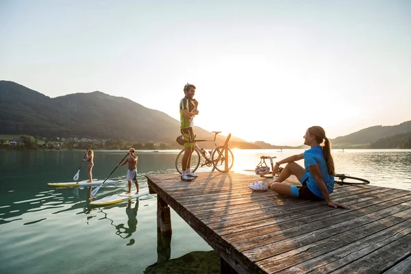 Österreich © Markus Greber Personen auf Steg und Stand-up-Paddle-Boards bei Sonnenuntergang am See