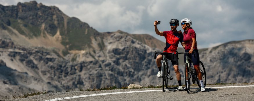 Nauders – Lago di Resia © Felix Saller Due ciclisti scattano un selfie su una strada di montagna con montagne sullo sfondo