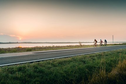 Emilia Romagna © Alex Moling Drei Radfahrer fahren bei Sonnenuntergang an einem Fluss entlang