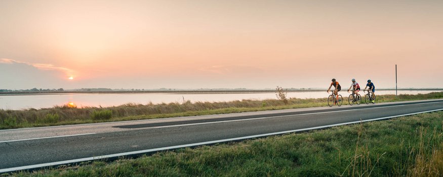 Adriatic coast © Alex Moling Three cyclists riding by a river at sunset