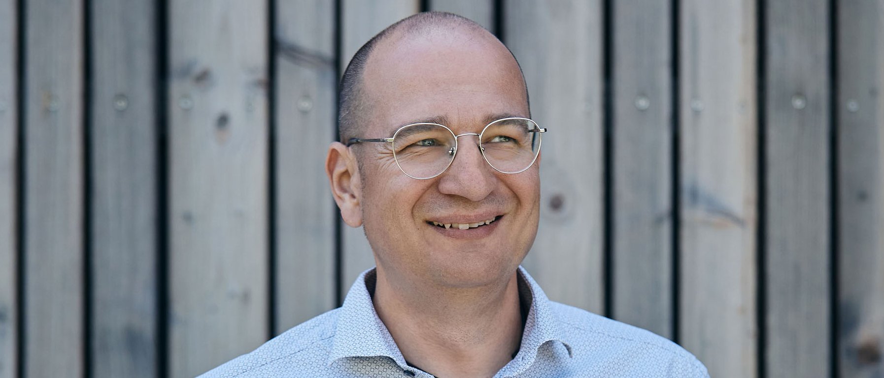 Landrefugium Obermüller – aktiver Rückzug im Rennradrefugium
© Landrefugium Obermüller Lächelnder Mann mit Brille vor Holzwand, Hände in den Hosentaschen