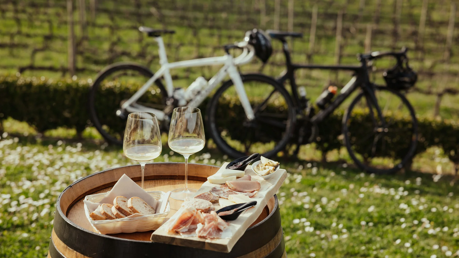 Roadbike Holidays © Alex Moling Weißwein, Brot und Aufschnitt auf Weinfass mit Fahrrädern im Hintergrund