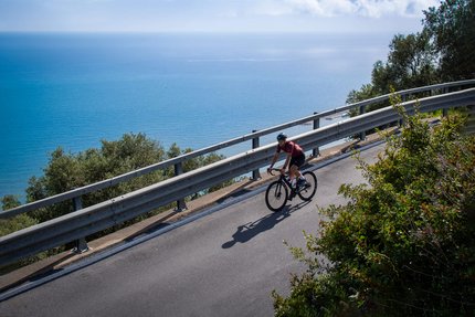 Ligurien © Valentina Morri Italy Radfahrer fährt eine Küstenstraße mit Blick auf das Meer entlang