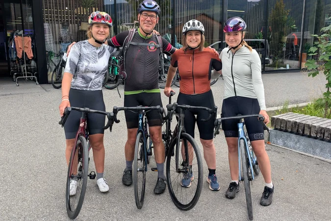 Roadbike Holidays Vier Radfahrer mit Helmen und Fahrrädern vor einem Gebäude mit großen Glasfenstern